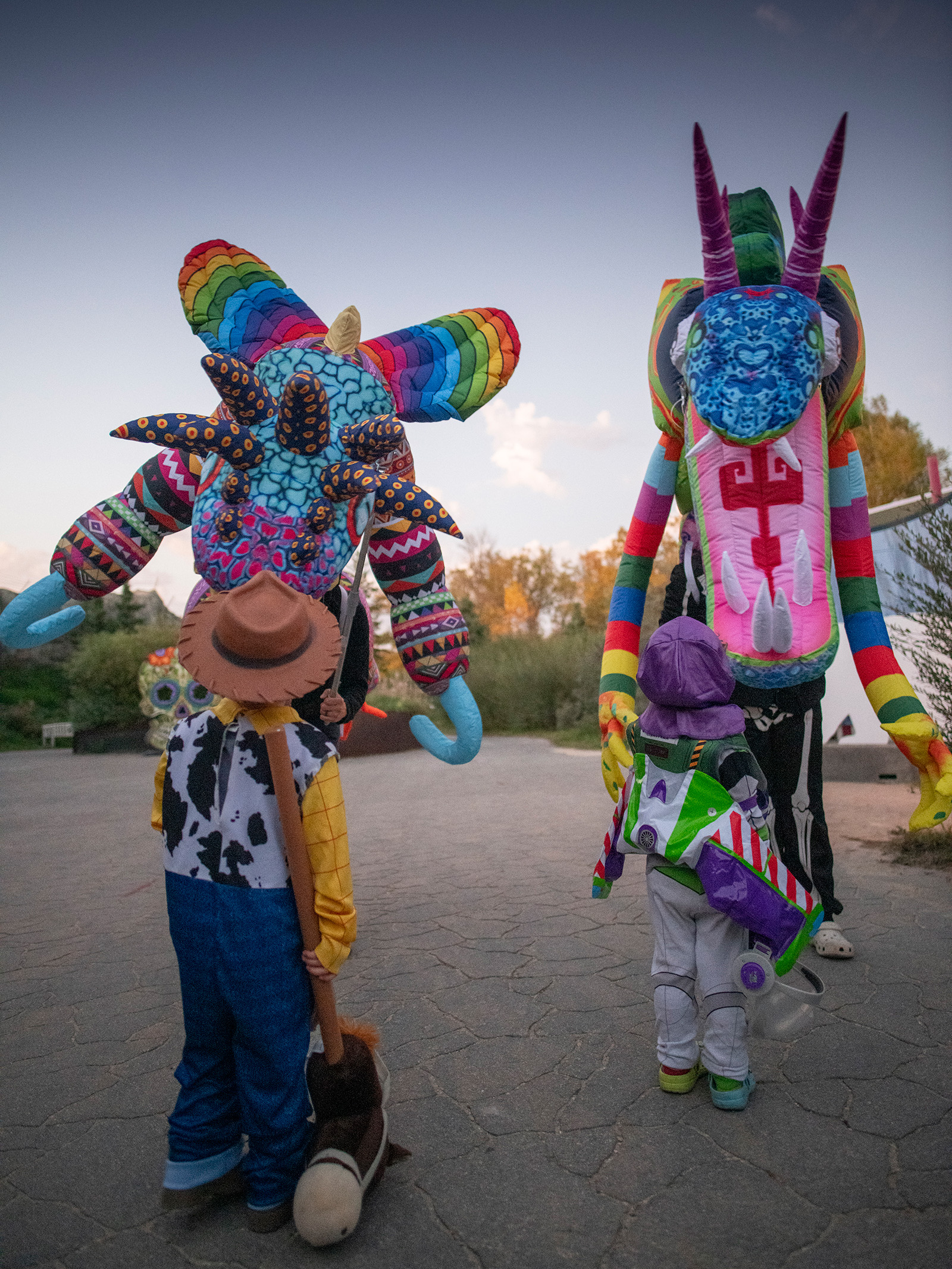 Two kids in costume look up towards colourful costumed creatures