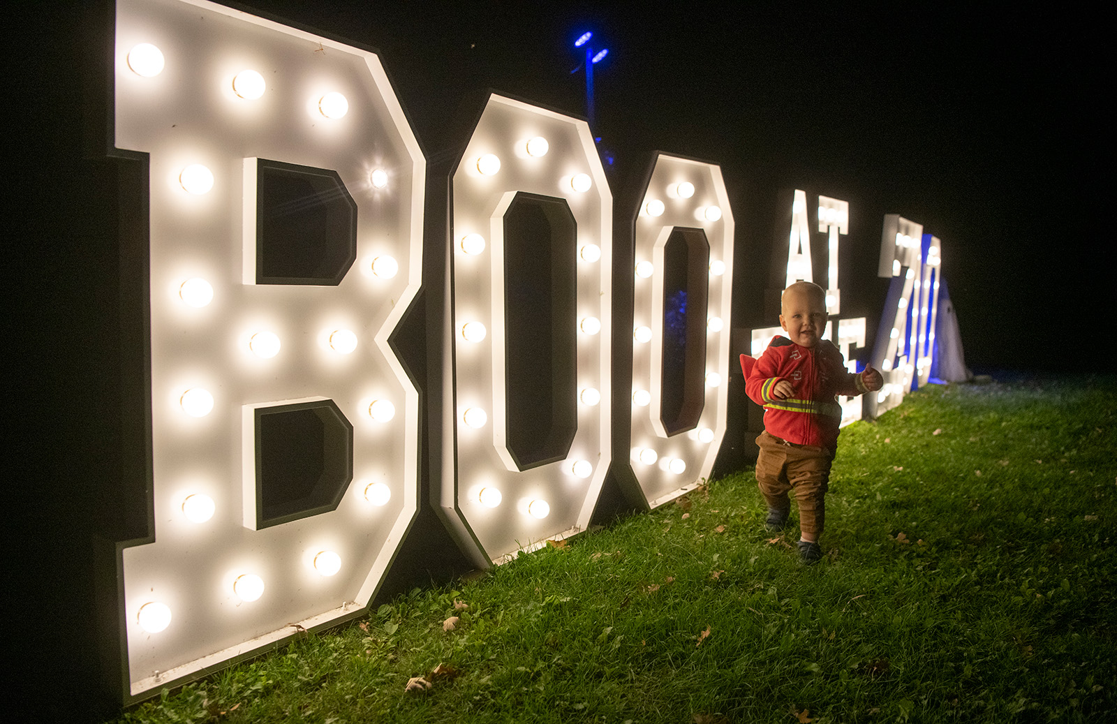 A toddler runs alongside a large lit sign that reads "Boo at the Zoo"