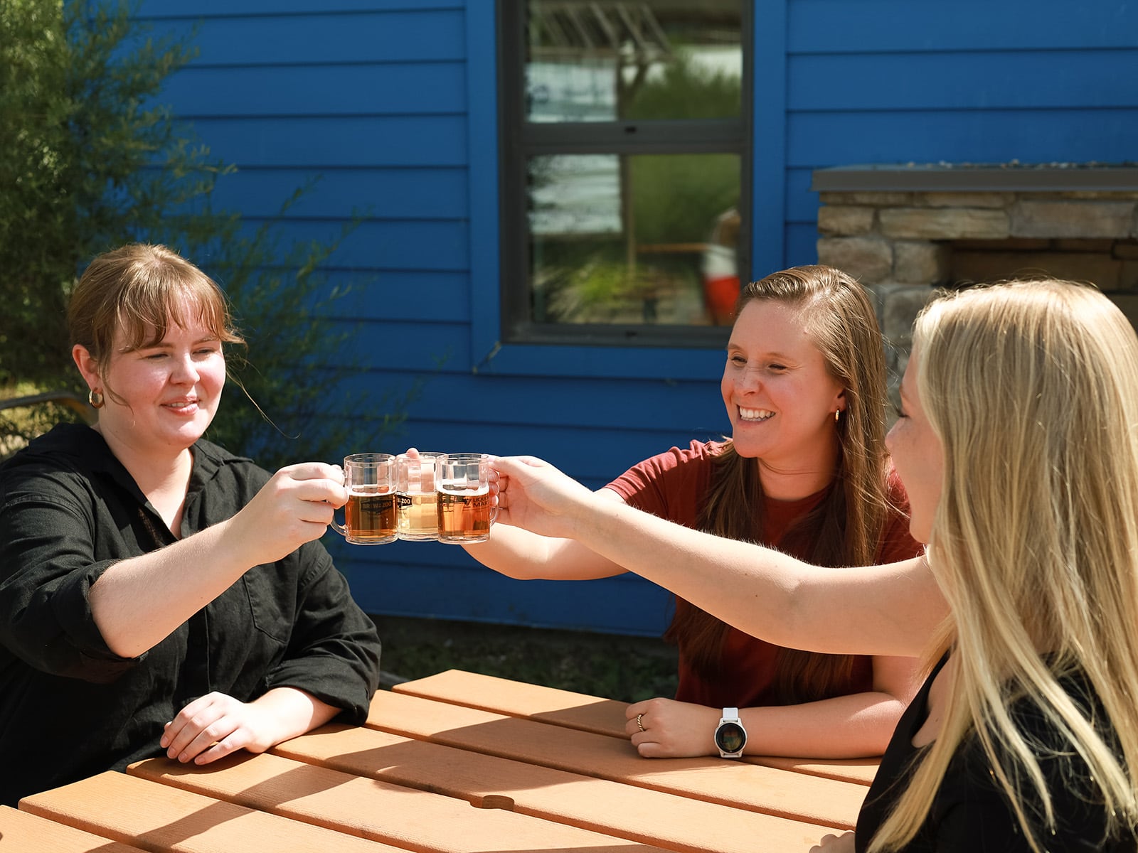 Three women sitting at a table cheers small sample beer glasses