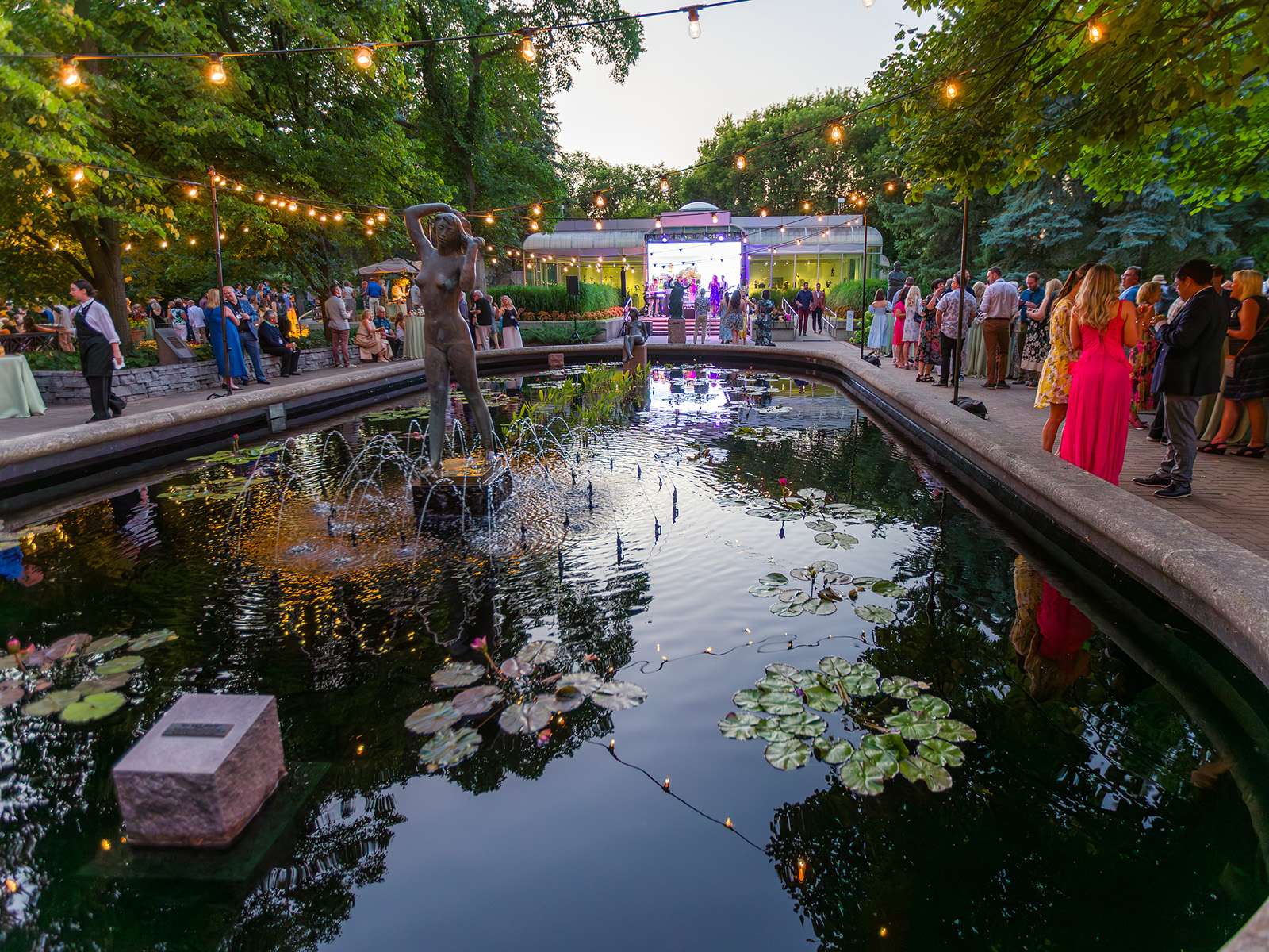 crowds of event guests mingle around the lily pond in the Leo Mol Sculpture Garden. 