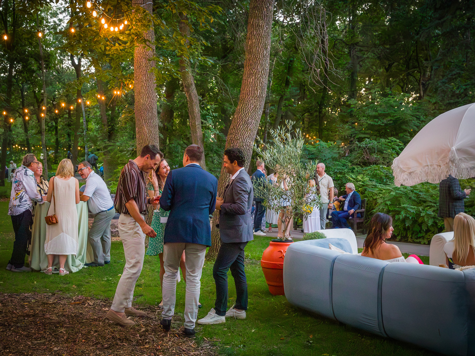 Small groups of event guests mingle on the lawn under trees in the Leo Mol Sculpture Garden