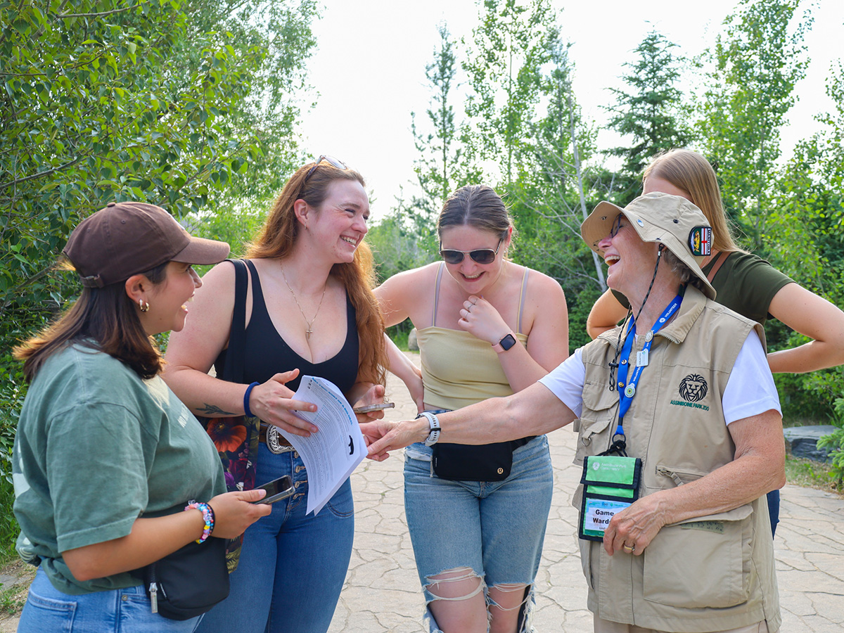 A uniformed game warden with a group of guests laugh and point at a game sheet