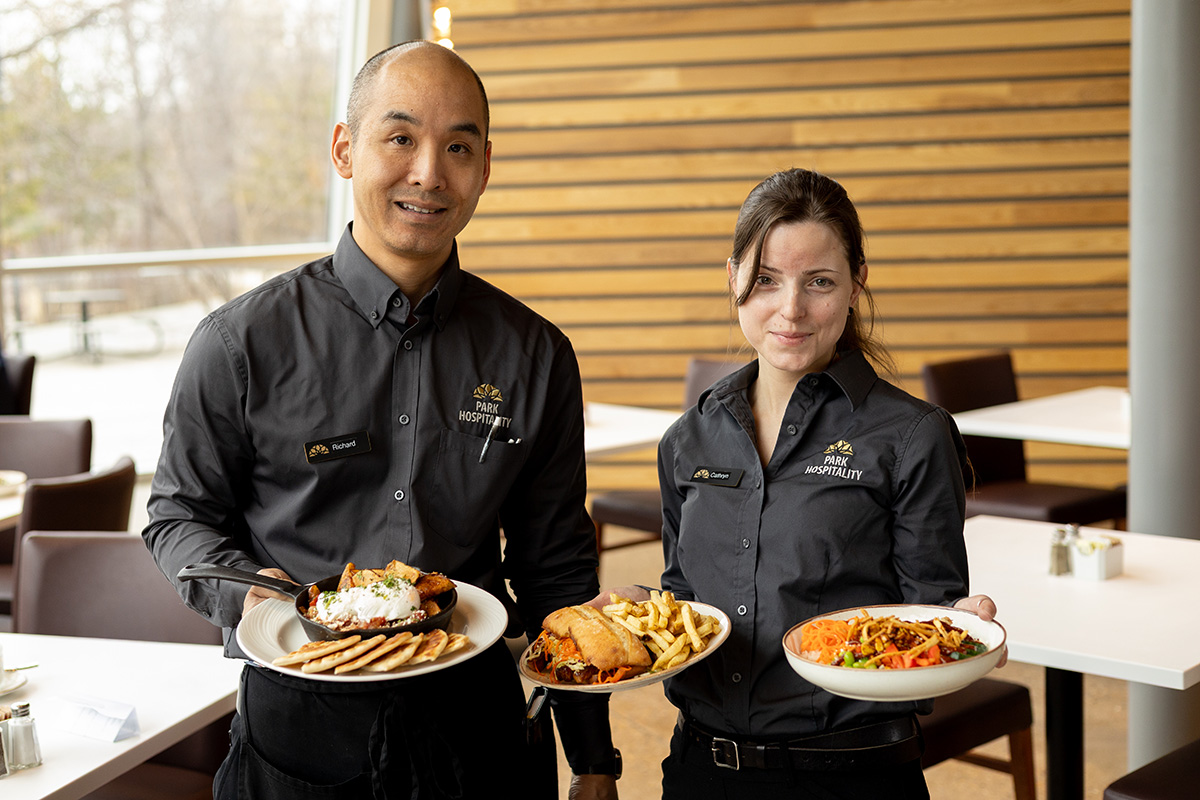 Two staff members at the Park Cafe hold up dishes of food
